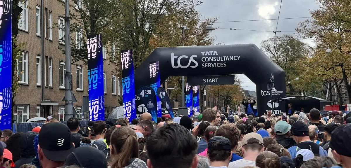 Runners waiting at the start arch of the Amsterdam TCS Marathon, under a grey sky